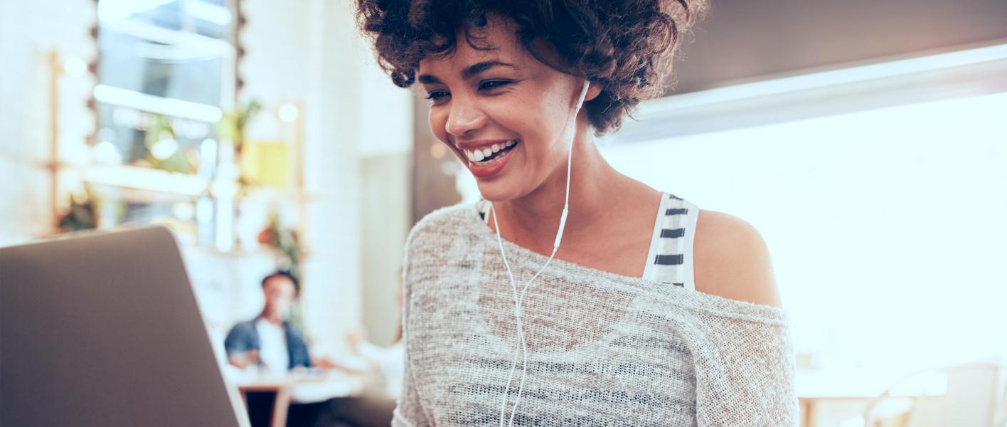 young woman wearing headphones happily working on laptop
