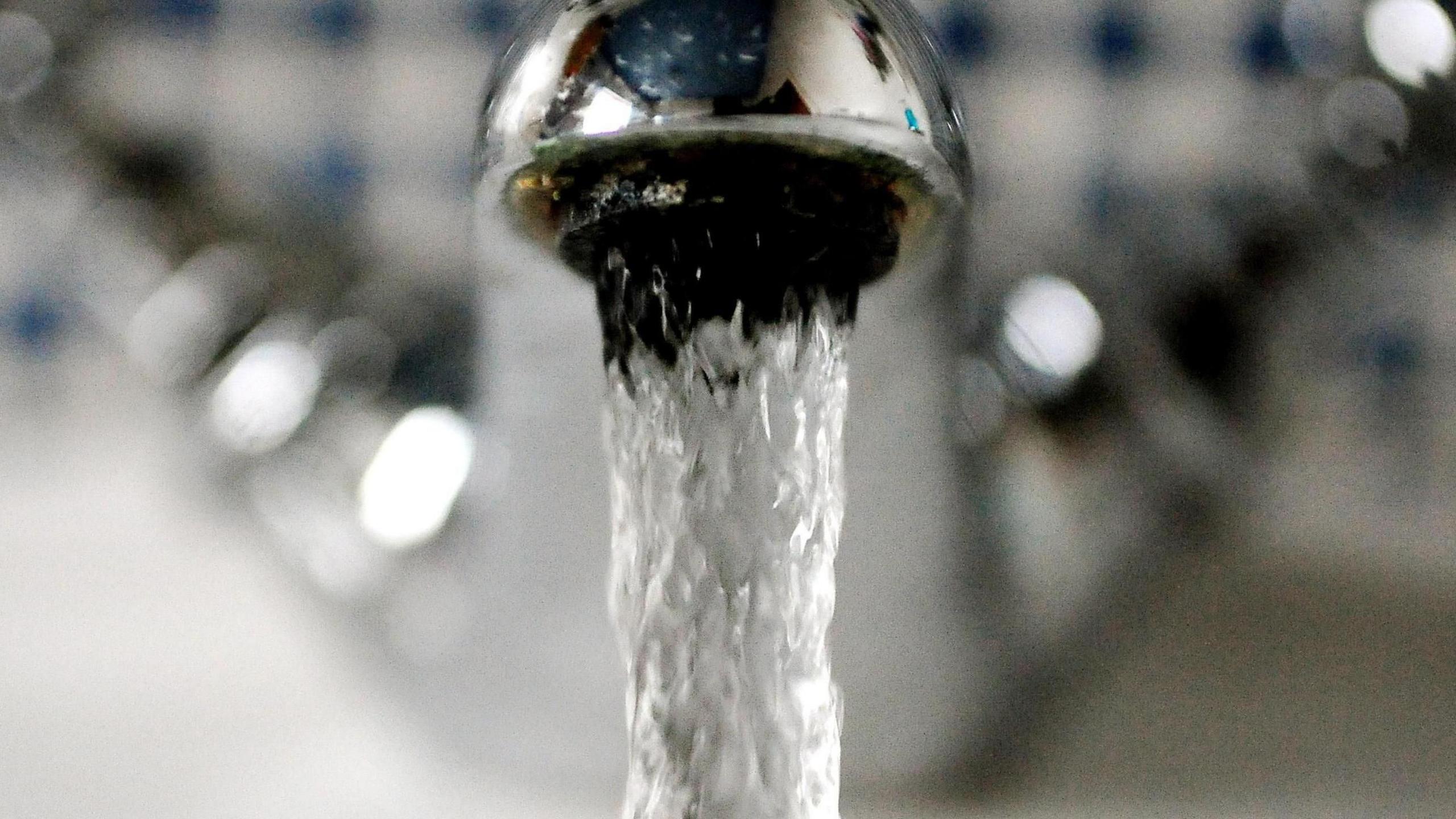 A close up of a silver-coloured tap with clear water pouring out of it.