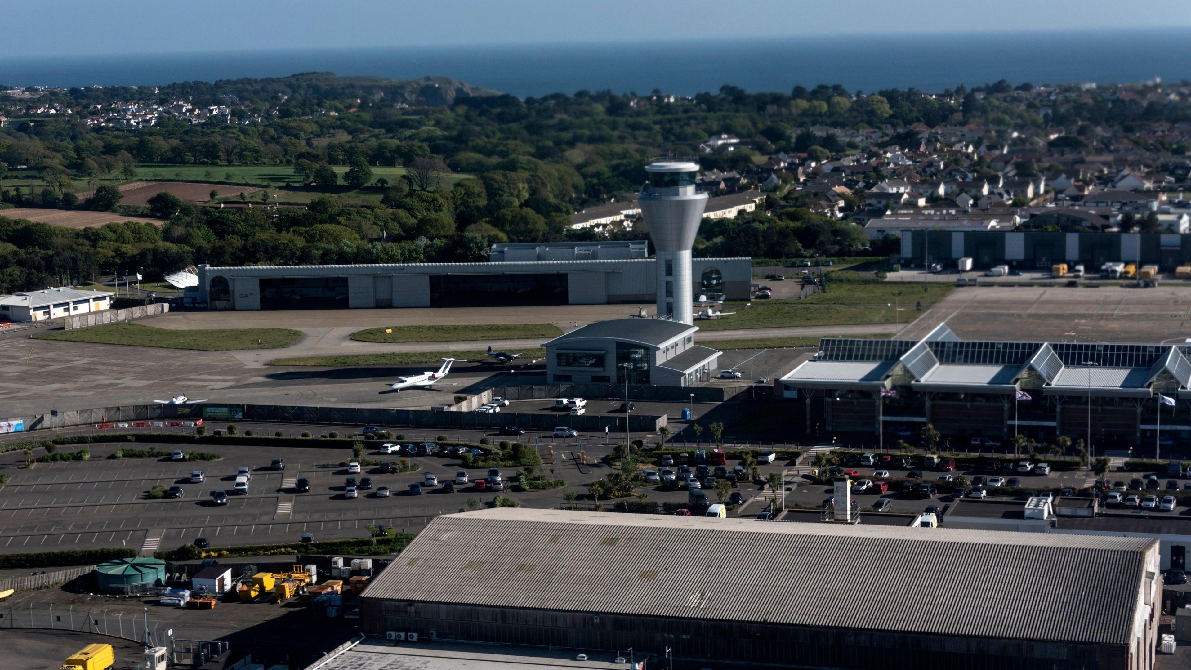 An aerial view of Jersey airport showing terminal buildings, control towers, runways and vehicles. 

