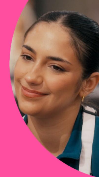 A young woman, Shakira Khan, has tied-back dark hair and is wearing a blue shirt with a white apron.