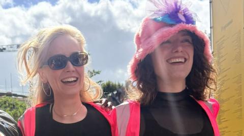 Two women who took part in a march to celebrate the new word for labia. They are both smiling. One wears a pink hat and both have bright pink jackets.