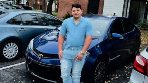 Perez leaning against a blue Honda car in a parking lot, smiling