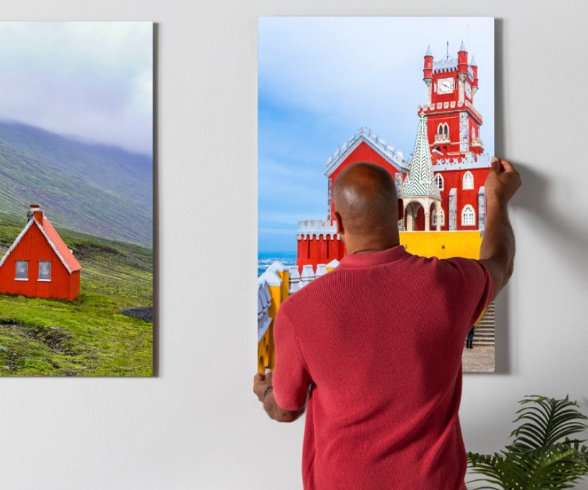 A man hanging a large canvas print of a colorful red and yellow castle onto a wall.